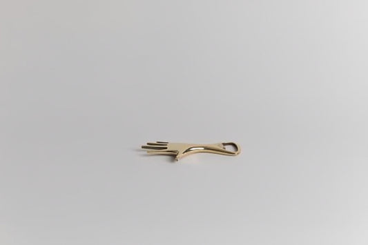 brass-colored hand shaped bottle opener on a light gray background